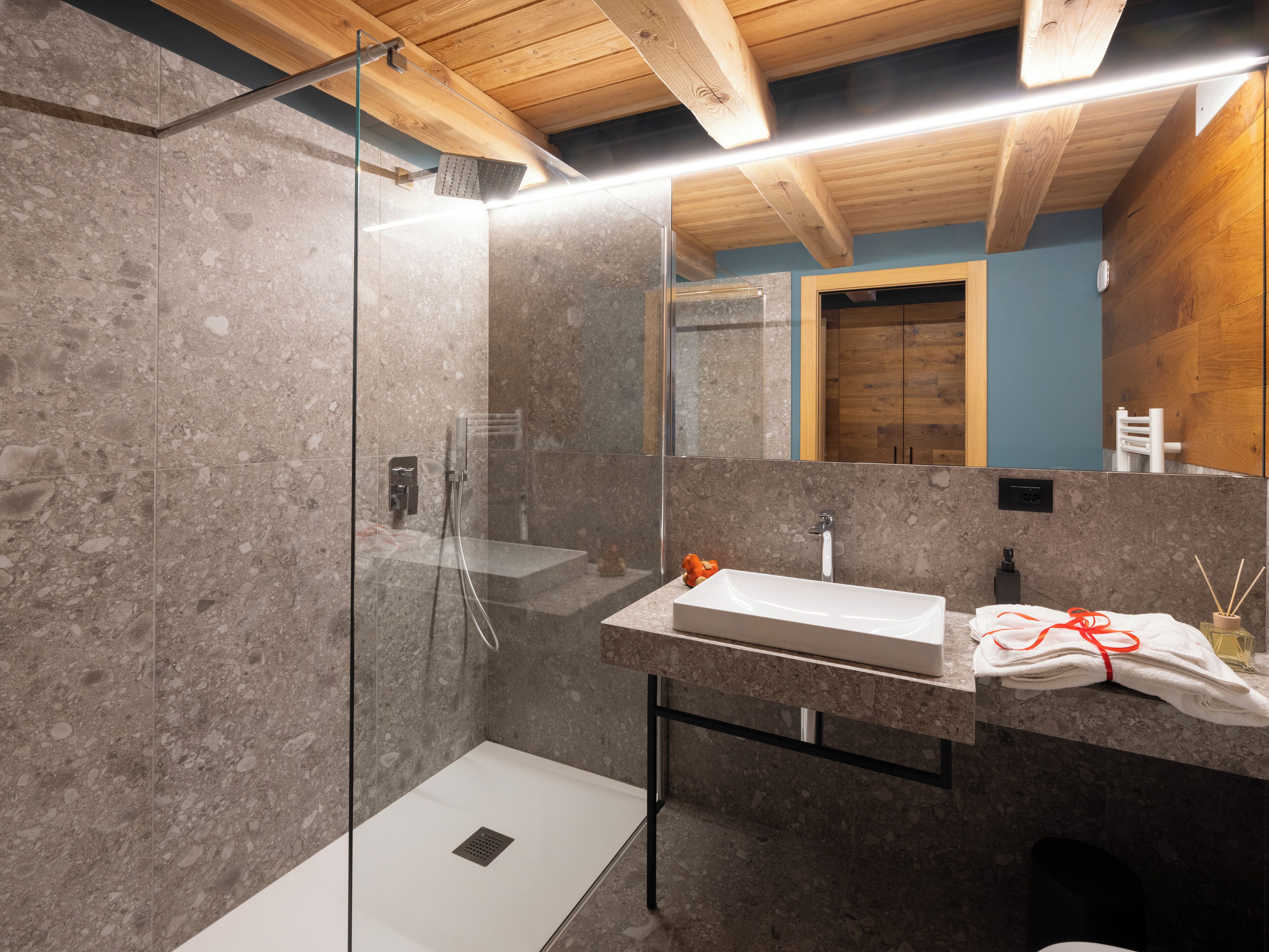 A modern bathroom with a glass-enclosed shower, a white sink, and a wooden ceiling.