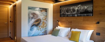 A bedroom with a bed, pillows, a painting of a mountain, and a wooden headboard.