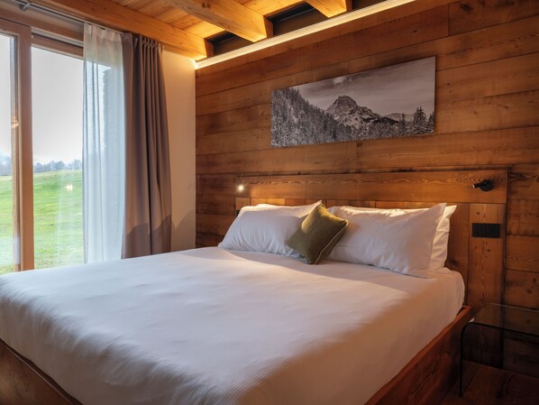 A wooden-paneled bedroom with a large bed, a painting of a mountain landscape, and a view of a green field through a window. - Chambre d' Hotes Vista Monte Bianco (La Salle)