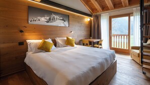 A bedroom with a wooden ceiling, a bed with white bedding and mustard pillows, a table with chairs, and a window with a view of the outdoors. - Chambre d' Hotes Vista Monte Bianco (La Salle)