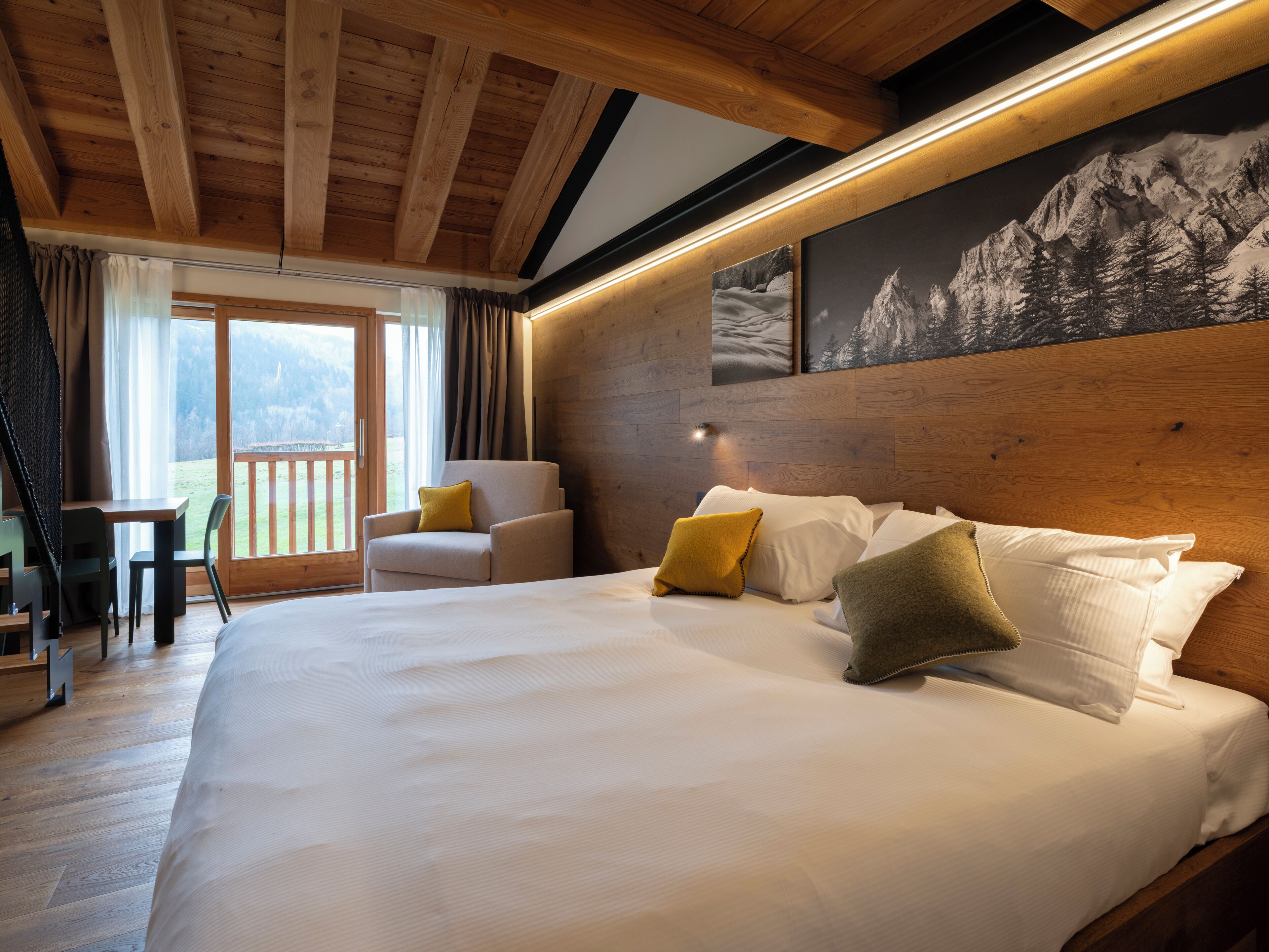 A bedroom with a large bed, a wooden headboard, a chair, and a view of the outdoors.