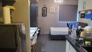 A compact kitchen with a dining area, a bed, and a small bathroom. - Cozy 1-bedroom condo with AC in charming Muntinlupa (Muntinlupa)