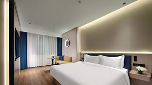 Habitación de hotel moderna con una cama grande, una mesita con un jarrón de flores y un sofá.