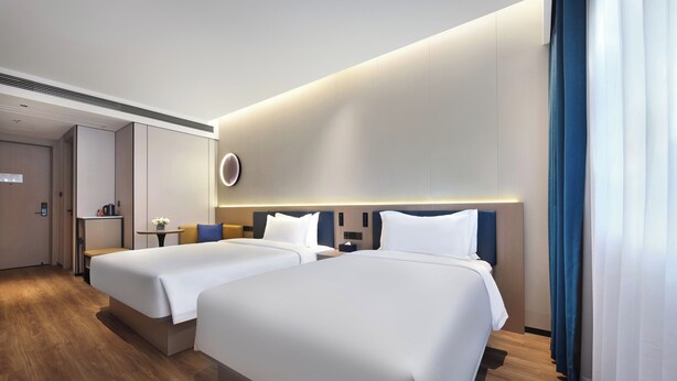 A modern hotel room with two beds, a small table with a vase, and a wall-mounted control panel. - Jinglai Zhenxuan Shanghai Tongji Hospital Xincun Road Subway Station Hotel (Shanghai)