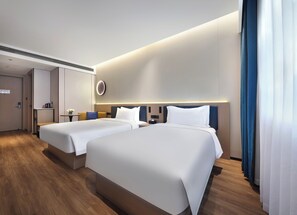 Ein modernes Hotelzimmer mit zwei Betten, einem kleinen Tisch mit einer Vase und einer an der Wand montierten Steuerung.