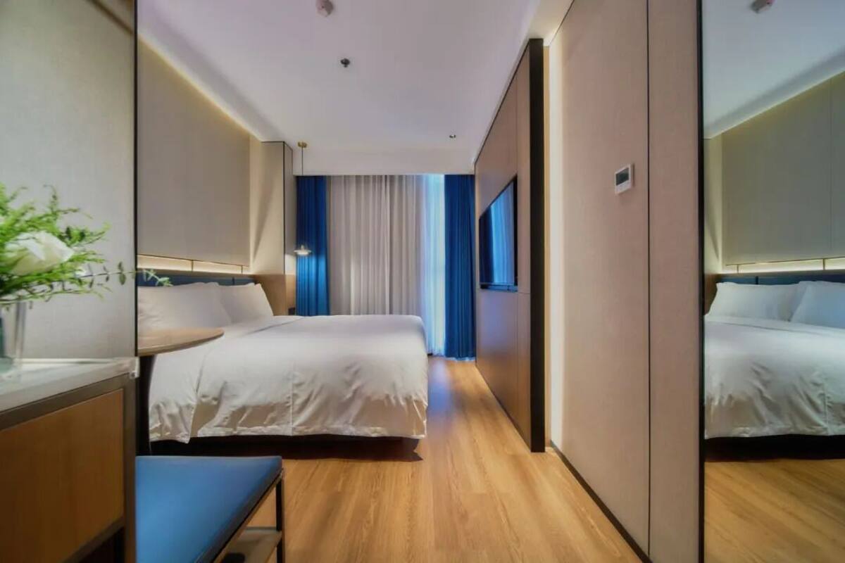 A hotel room with a bed, bedside table, and a mirror.