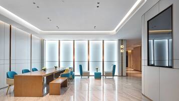 A modern conference room with a long table, blue chairs, and a large screen on the wall.