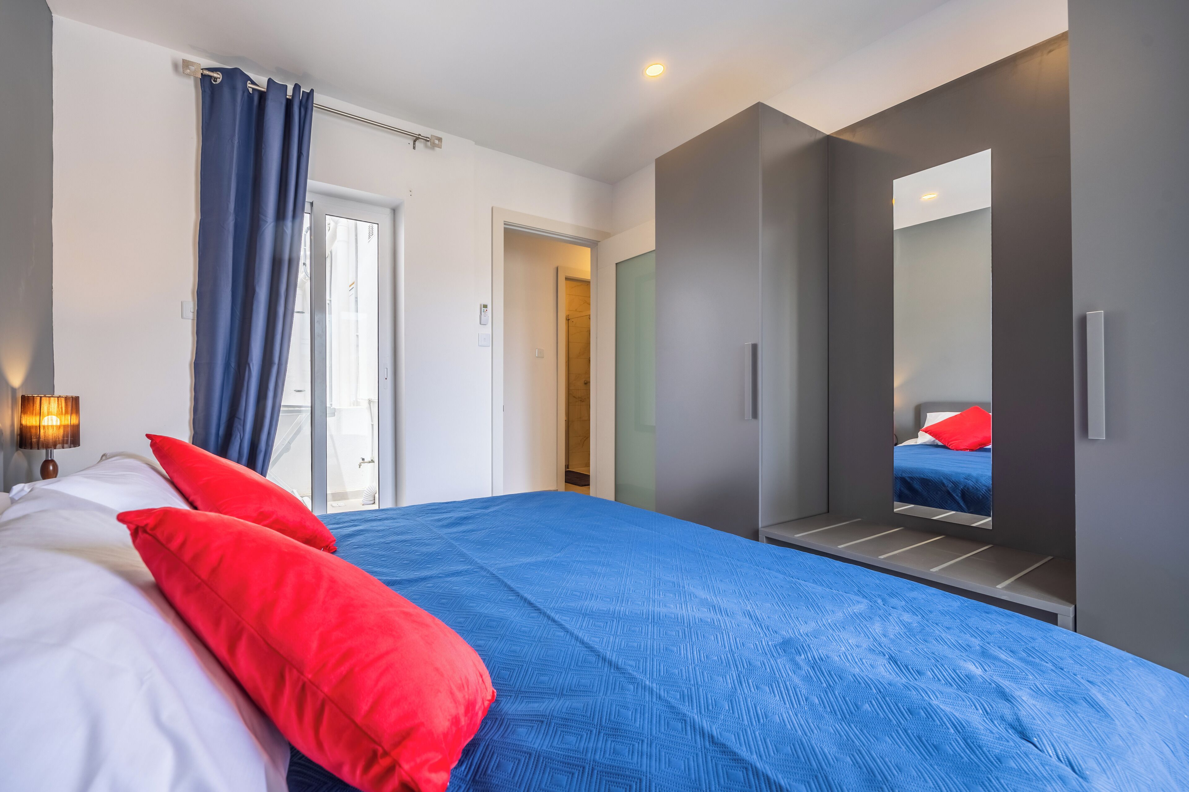 Una habitación de hotel moderna con una cama grande, un espejo y vistas al pasillo.
