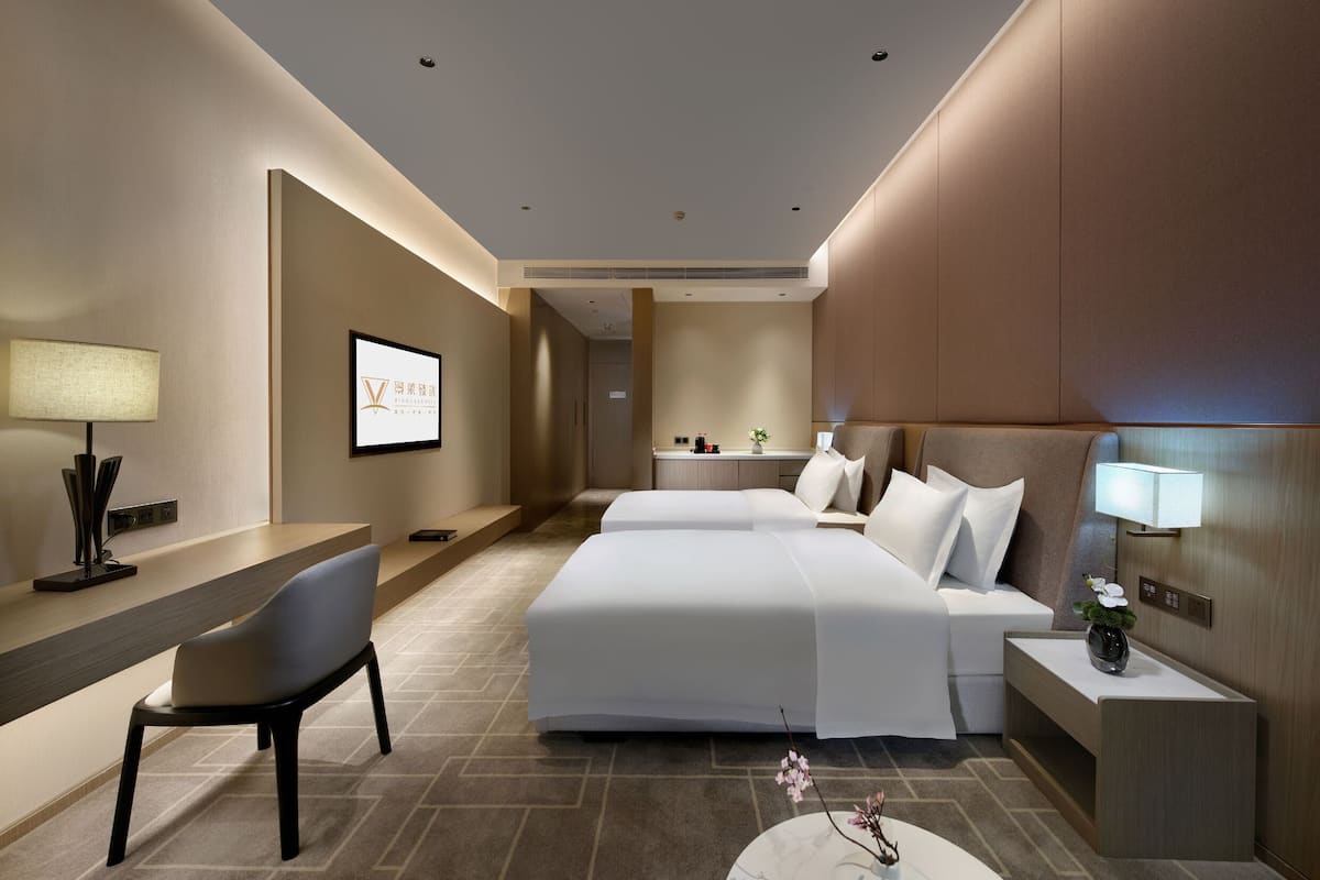 Una habitación de hotel moderna con cama, mesita de noche, lámpara, escritorio, silla y un cuadro en la pared.