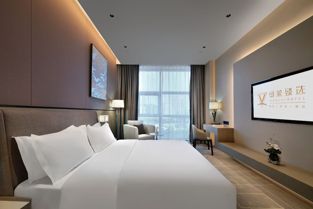 Una habitación de hotel moderna con una cama grande, un escritorio, una silla, un televisor y una ventana con cortinas.