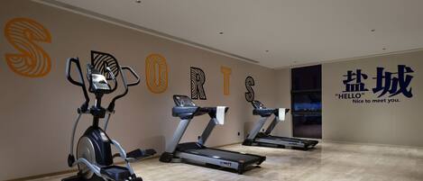 Un gimnasio con tres cintas de correr, una bicicleta estática y una pared con letras grandes que dicen "SPORTS".