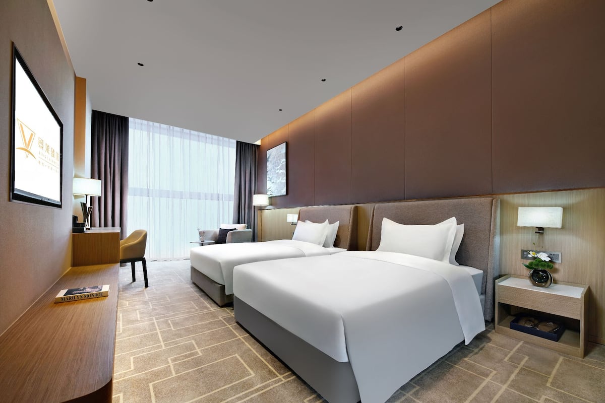 Habitación de hotel con dos camas, un escritorio, una silla, un televisor y una ventana con cortinas.