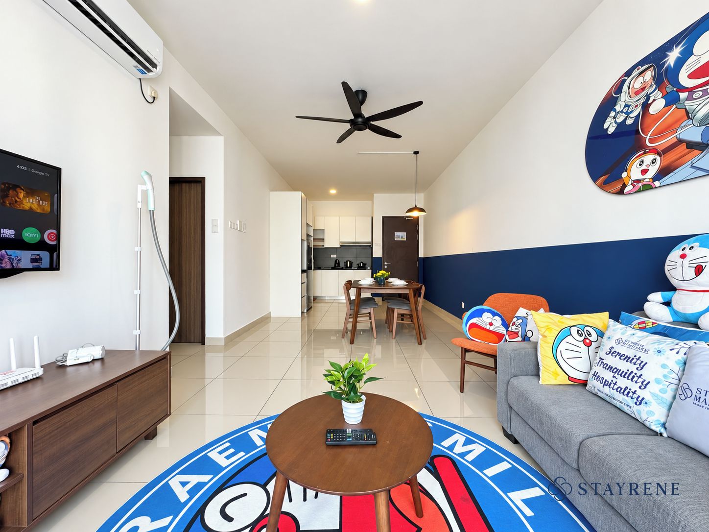 A modern living room with a TV, a ceiling fan, a dining area, and a sofa with colorful cushions.