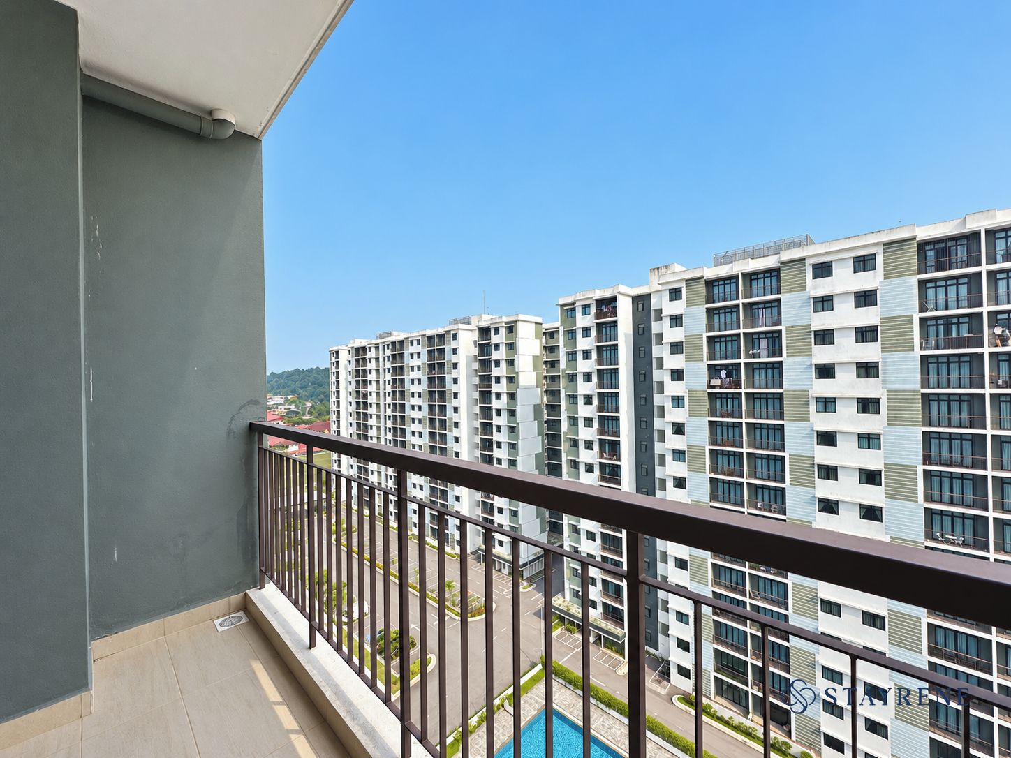 Un balcón con vistas a edificios residenciales altos, cielo despejado y una piscina al frente.