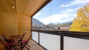 Un balcón de madera con una mesa y sillas, con vistas a un paisaje montañoso con casas y árboles otoñales.