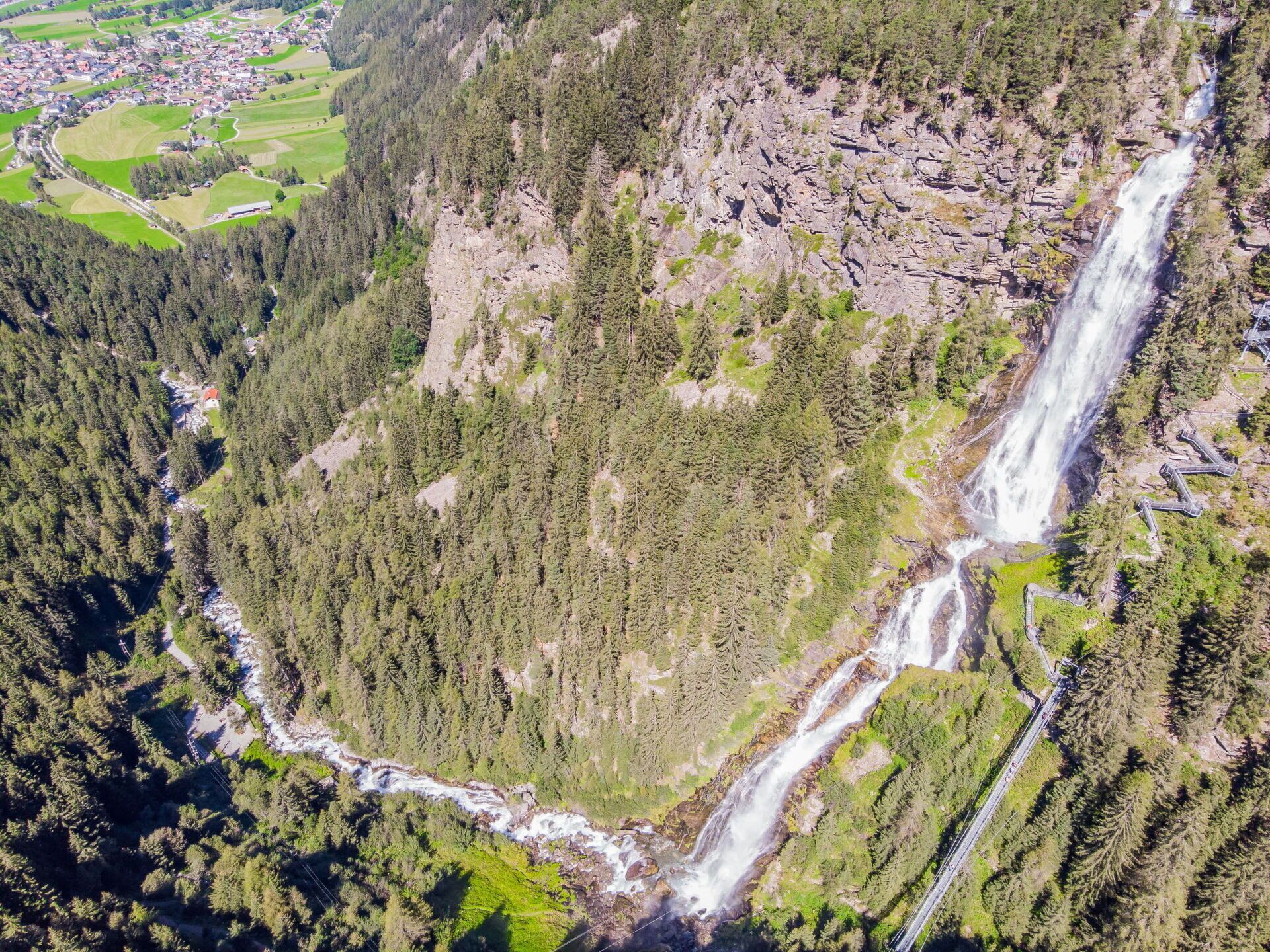 A mountainous area with a waterfall, dense forest, and a small settlement in the valley.