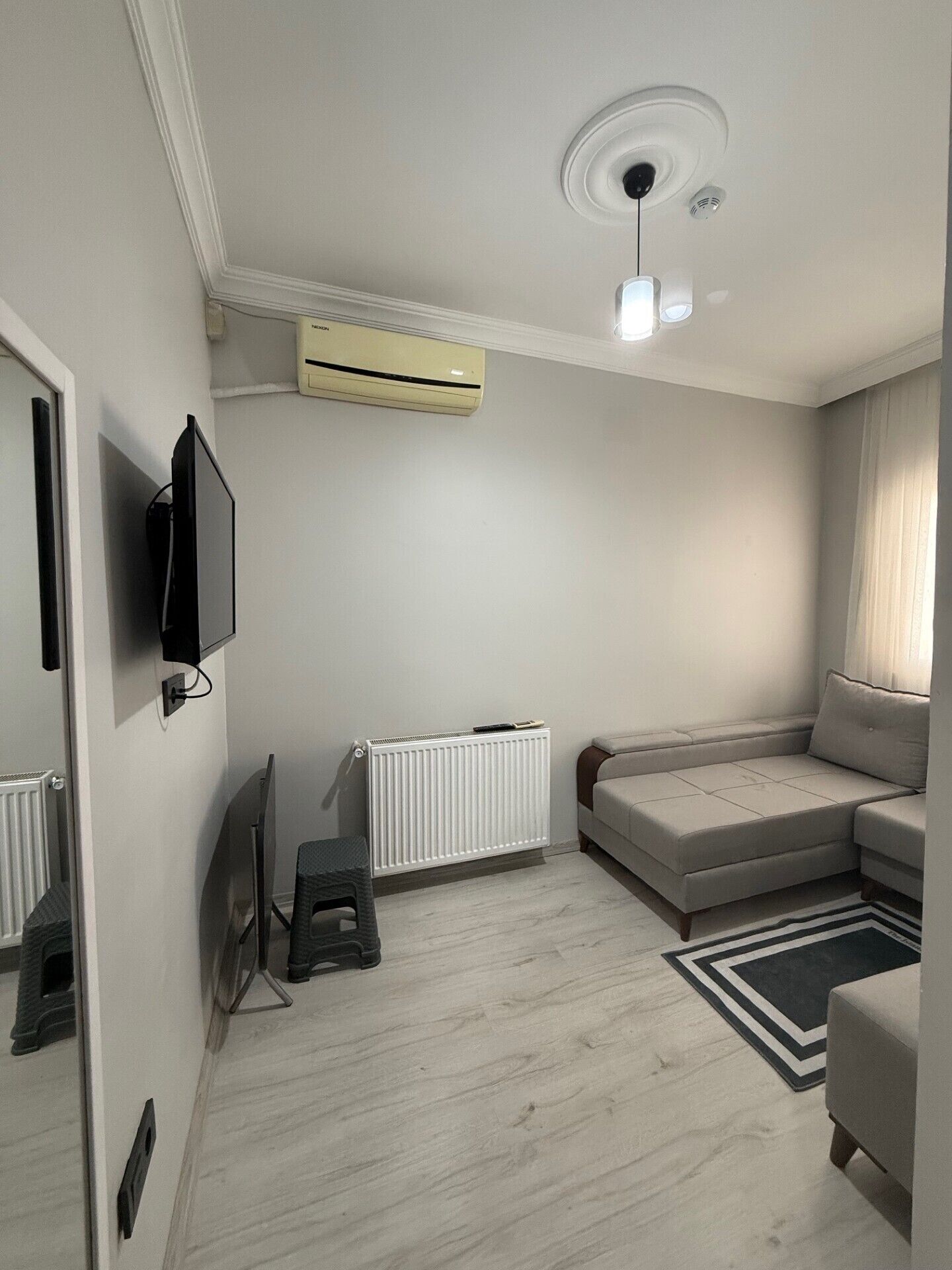 A modern living room with a sofa, a television, a radiator, and a ceiling fan.