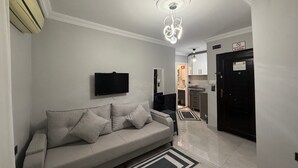 Uma sala de estar com sofá, televisão de tela plana e um lustre moderno.
