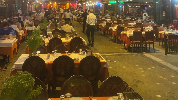 Rua movimentada com restaurantes e mesas ao ar livre, dispostas para os clientes.