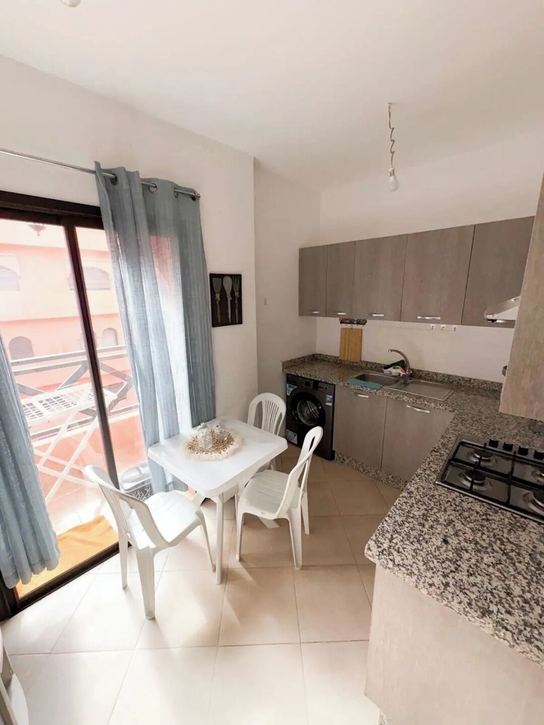 A compact kitchen with a gas stove, a washing machine, and a dining area with a table and chairs.