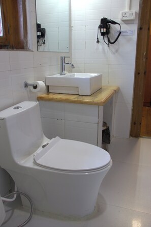A bathroom with a white toilet, a wooden vanity, a mirror, and a wall-mounted camera. - Kaila Guest House (Bumthang)