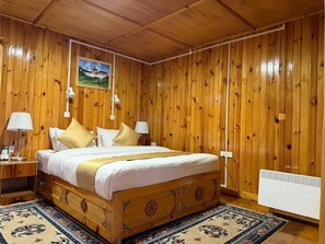 Ein Zimmer mit Holzwänden, einem Bett, Nachttischen, Lampen, einem Heizkörper und einem gerahmten Bild an der Wand.