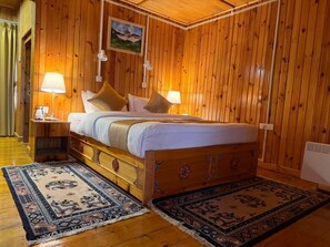 A wooden-paneled room with a bed, two bedside lamps, a nightstand, a painting, and two rugs. - Kaila Guest House (Bumthang)