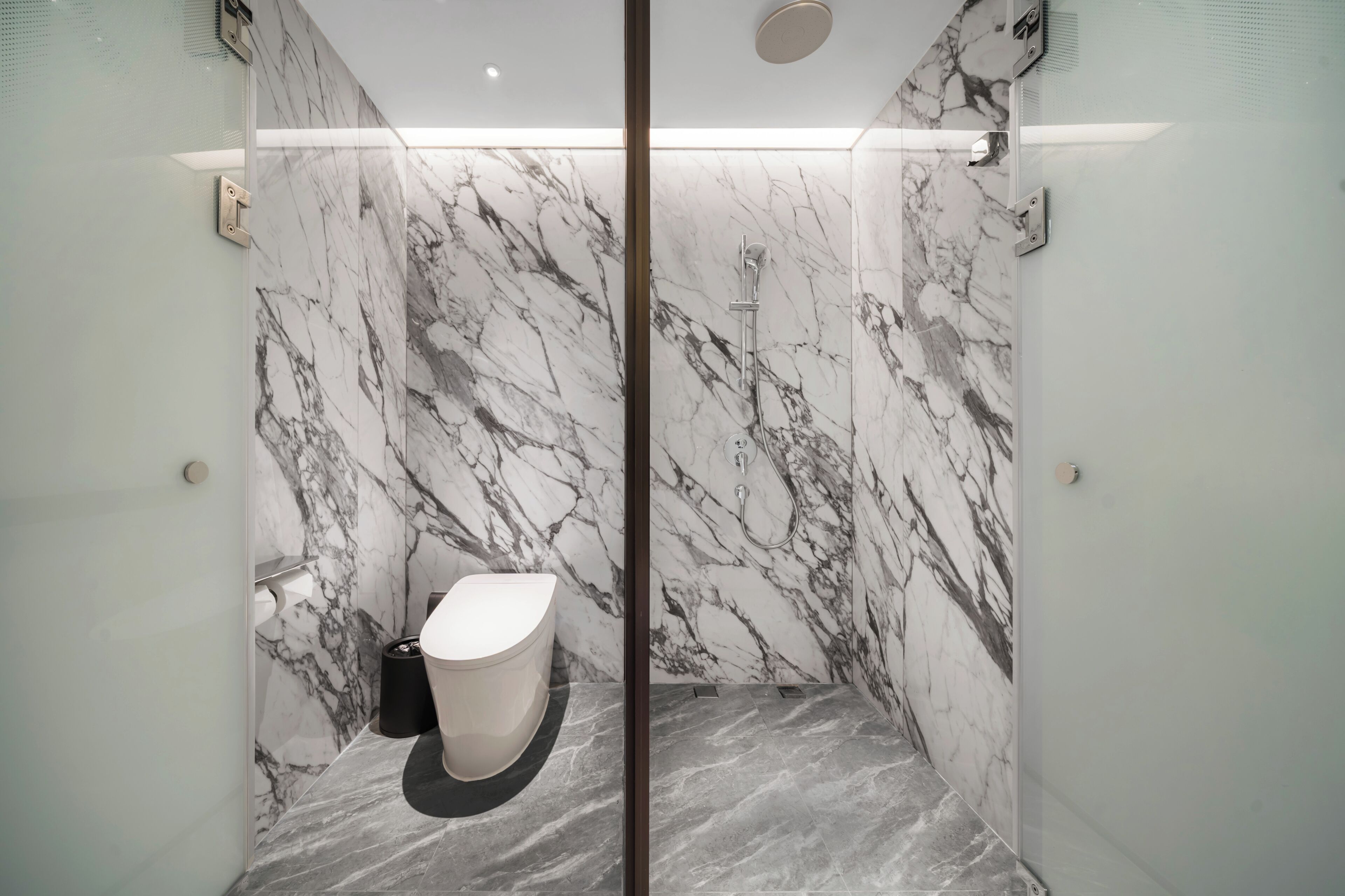 A modern bathroom with marble walls, a toilet, and a shower.