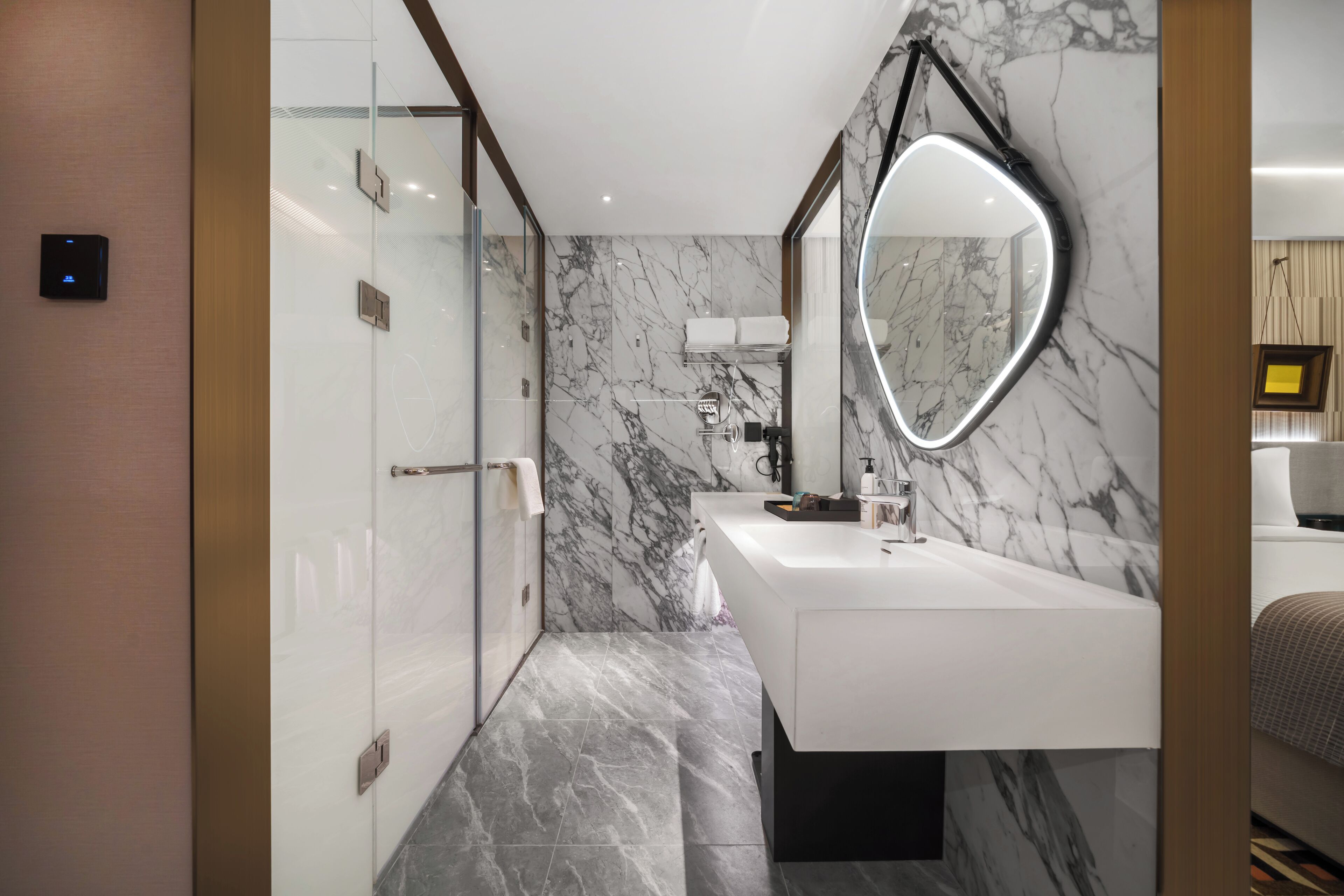 A modern bathroom with a marble wall, a large mirror, and a white sink.