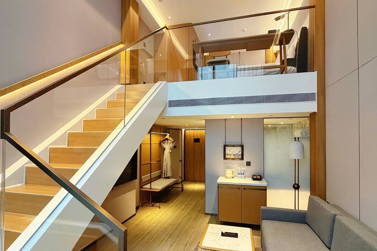 A modern interior with a staircase, a mezzanine level, a sofa, a coffee table, and a small table with a lamp.