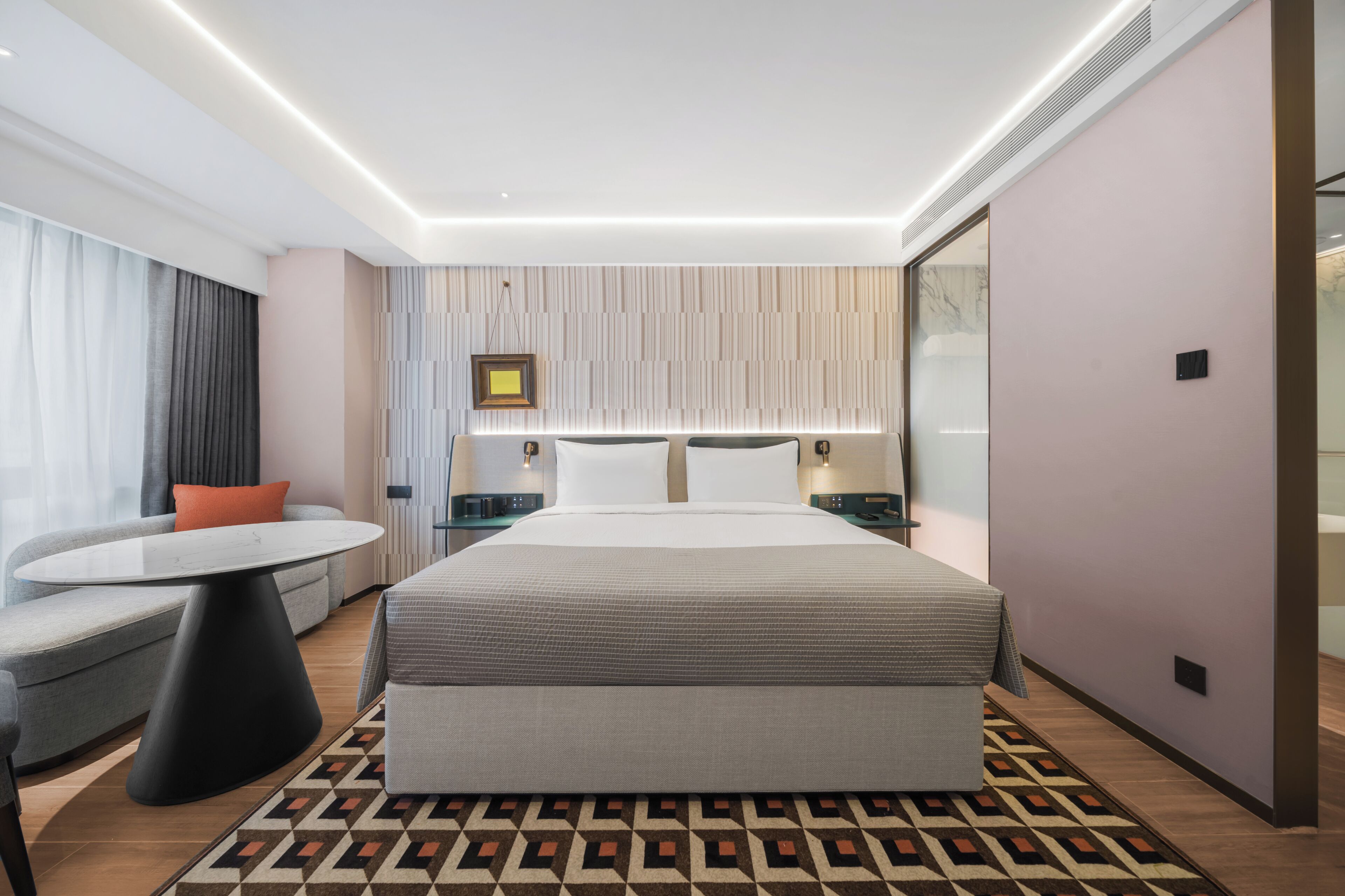 A modern hotel room with a large bed, a sofa, a small table, and a patterned rug.