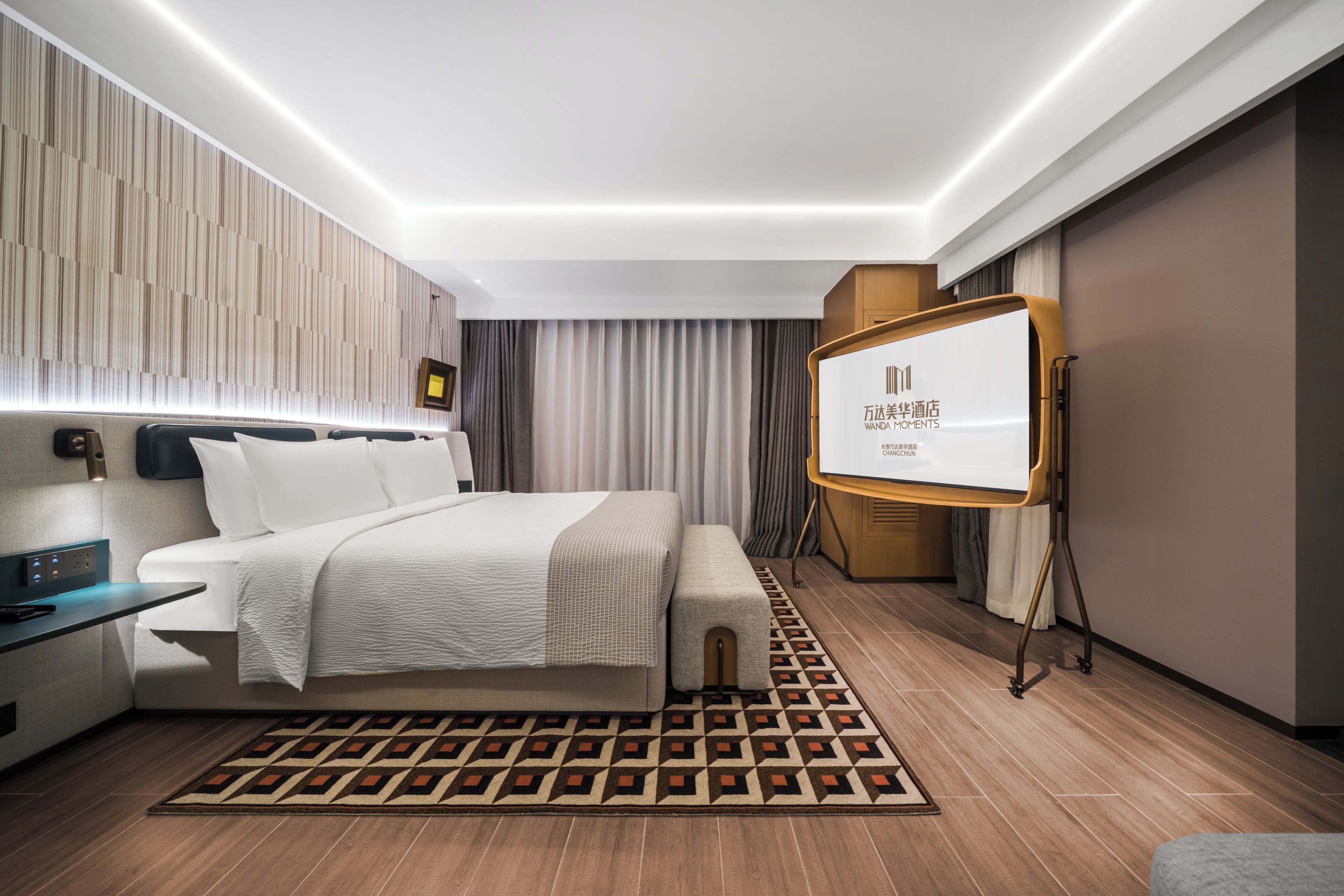 Una habitación de hotel moderna con cama, mesita de noche, televisor y alfombra estampada.