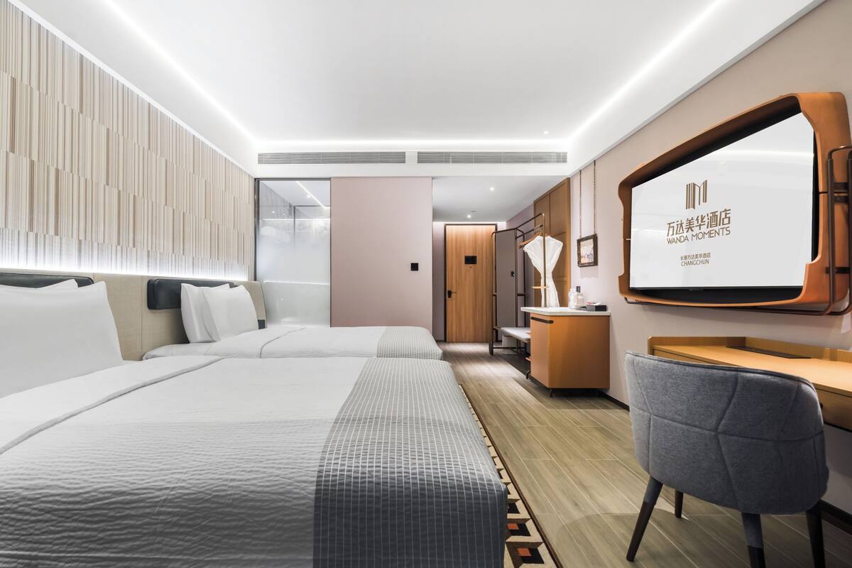 A hotel room with two beds, a desk, a chair, and a large mirror.