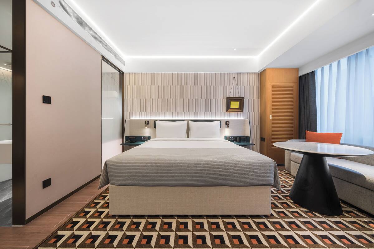 A modern hotel room with a large bed, bedside tables, a round table, and a sofa.