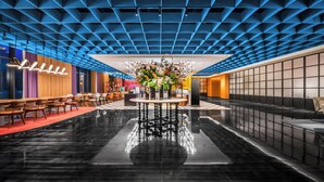 A modern lobby with a reflective floor, a central floral arrangement, and a blue patterned ceiling. - Wanda Moments Changchun (Changchun)