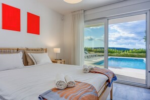 Ein Hotelzimmer mit Bett, Nachttisch, Lampe und Blick auf einen Swimmingpool sowie zwei rote Wandbilder.