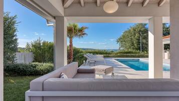 Zona junto a la piscina con sofás y sillones reclinables, una palmera y vistas a la piscina y al paisaje.