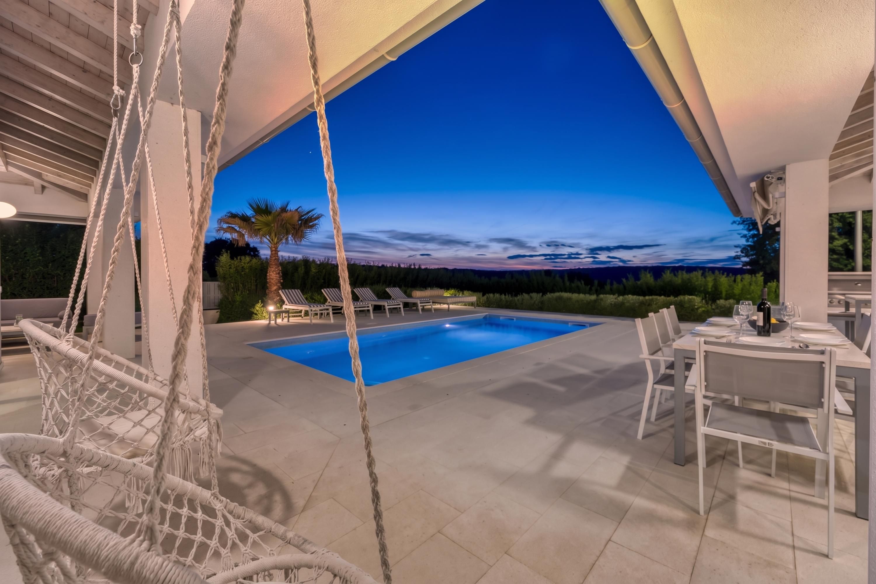 A pool area with a swing chair, lounge chairs, and a dining table set for a meal.