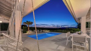A pool area with a swing chair, dining table, and chairs, under a covered patio. - Pool Villa Ora in Nature (Marcana)