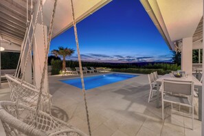 A pool area with a swing chair, dining table, and chairs, under a covered patio. - Pool Villa Ora in Nature (Marcana)