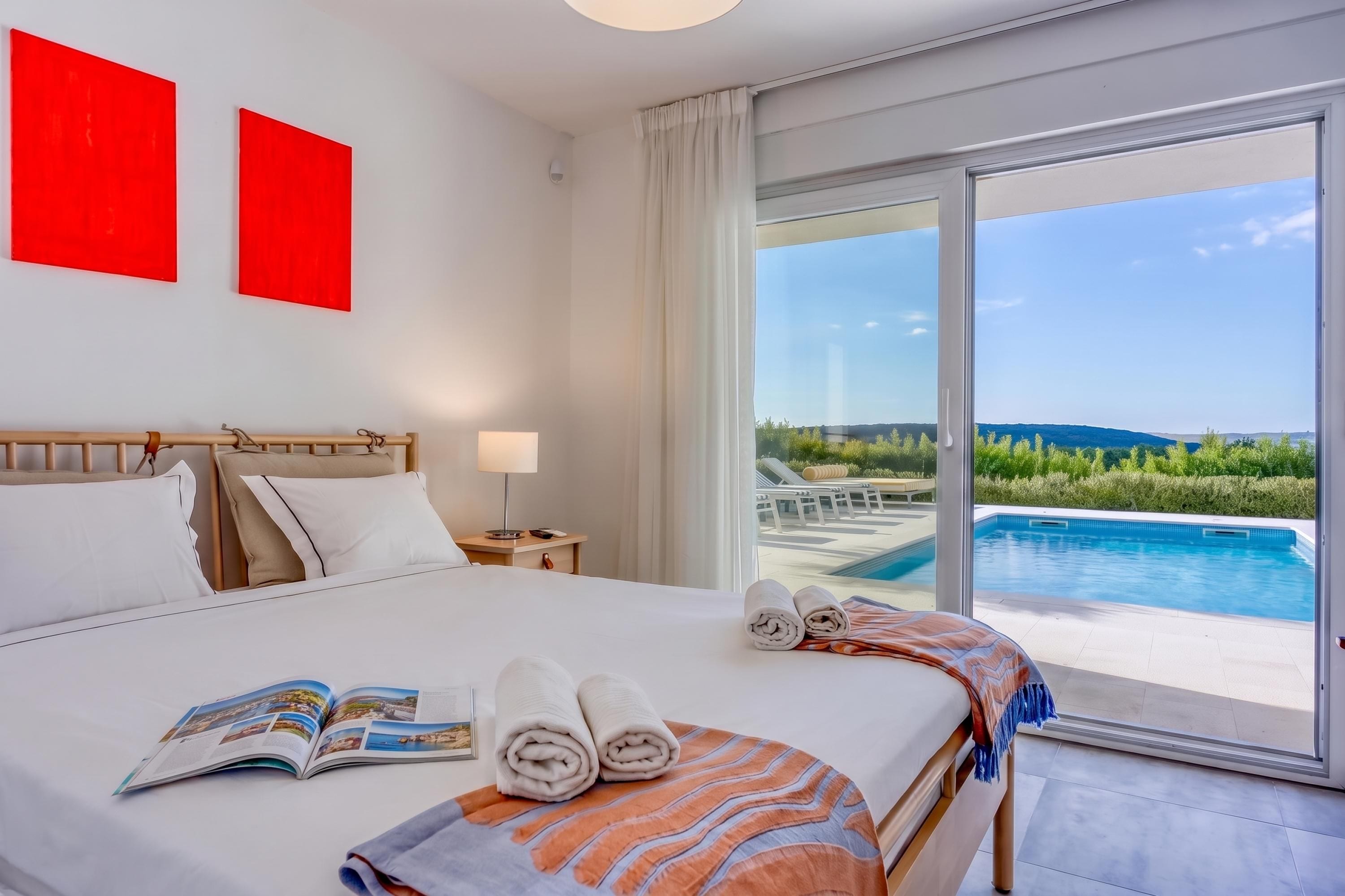 Habitación de hotel con una cama grande, vista a una piscina y dos obras de arte rojas en la pared.