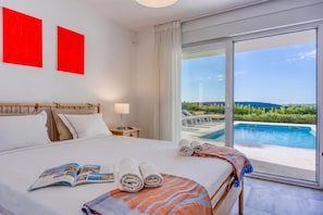 A hotel room with a large bed, a view of a swimming pool, and two red artworks on the wall. - Pool Villa Ora in Nature (Marcana)