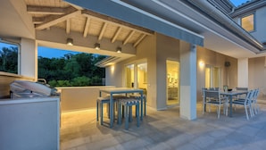 An outdoor patio area with a table and chairs, a grill, and a covered seating area. - Pool Villa Ora in Nature (Marcana)
