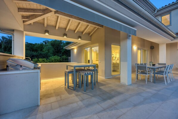 An outdoor patio area with a table and chairs, a grill, and a covered seating area. - Pool Villa Ora in Nature (Marcana)