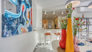 Une cuisine moderne avec des meubles blancs, un coin repas doté d’une table ronde et une peinture abstraite aux couleurs vives accrochée au mur.