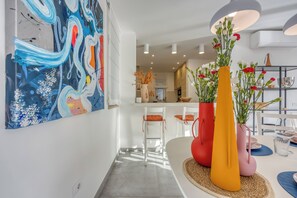 A modern kitchen with white cabinets, a dining area with a round table, and a colorful abstract painting on the wall. - Pool Villa Ora in Nature (Marcana)