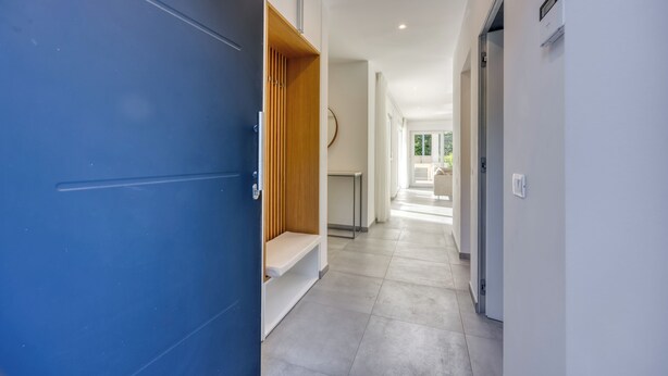 Un couloir avec une porte bleue, un banc en bois, un mur blanc et un luminaire au plafond.