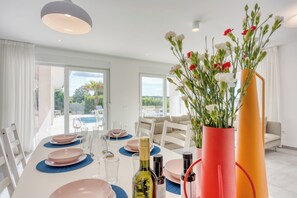 A dining area with a table set for four, a bottle of wine, and a vase with flowers. - Pool Villa Ora in Nature (Marcana)