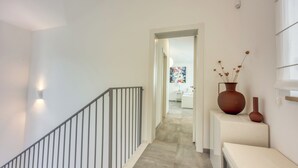 Un couloir avec un escalier, un mur blanc et une porte donnant sur une autre pièce.