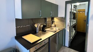 A compact kitchen with dark cabinets, a sink, and a countertop. There is a small dining area with a table and a chair. - Studio cabin at the foot of the slopes - Valfréjus (Valfréjus)